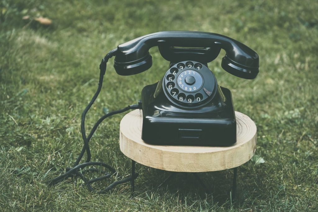 Mastering the First Impression: Your intriguing post title goes here A classic black rotary phone displayed on a wooden stand outdoors on grass.